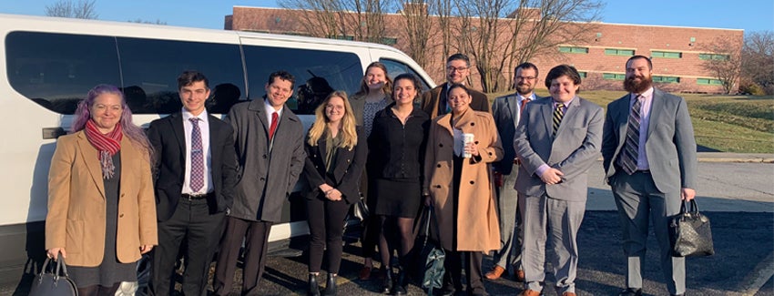 A group of students, faculty,and advisors pose for an image outside in front of a van.