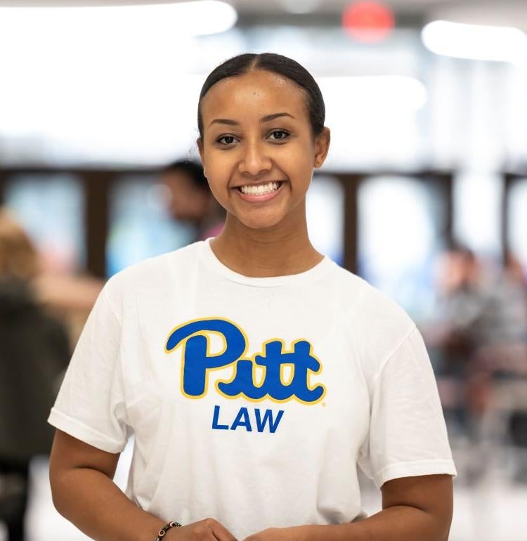 Woman smiling and standing in the middle of a room with a white Pitt Law shirt